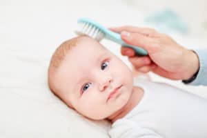 Baby bekommt die Haare gekämmt, um Schuppe zu entfernen.