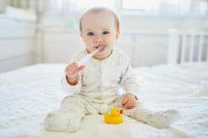 Baby sitzt auf dem Bett und hat eine Zahnbürste im Mund