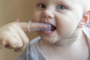 Baby bekommt von seiner Mutter die Zähne mit einer Silikon Zahnbürste geputzt.