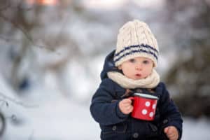 Kleinkind steht draußen im Schnee und trinkt warmen Kakao