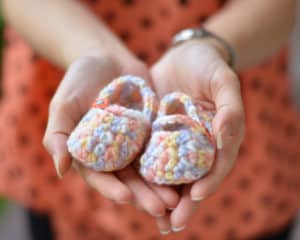Frau hält bunte Babyschuhe, die sie selber gehäkelt hat