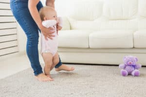 Mutter hält Baby unter den Armen und unterstützt es beim Laufen