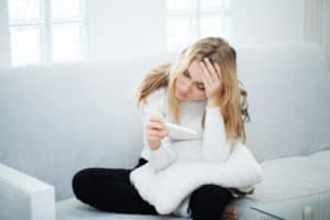 traurige Frau sitzt auf dem Sofa und hält negativen Schwangerschaftstest in der Hand