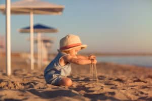 Kleinkind sitzt am Strand und spielt