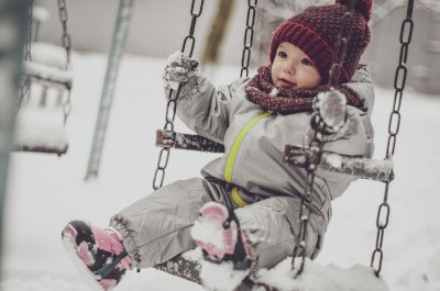 Kleinkind sitzt mit Schneeanzug in einer Schaukel