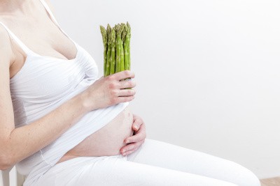 Schwangere Frau hält grünen Spargel in einer Hand