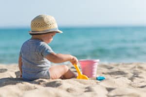 Kleinkind sitzt am Strand und spielt mit seinem Sandspielzeug